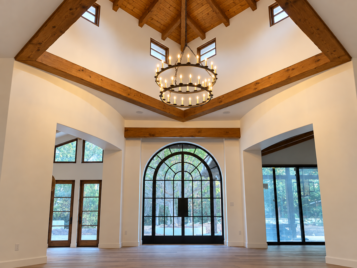 Warm two-tier chandelier beneath a timber ceiling, centered above an arched glass entryway